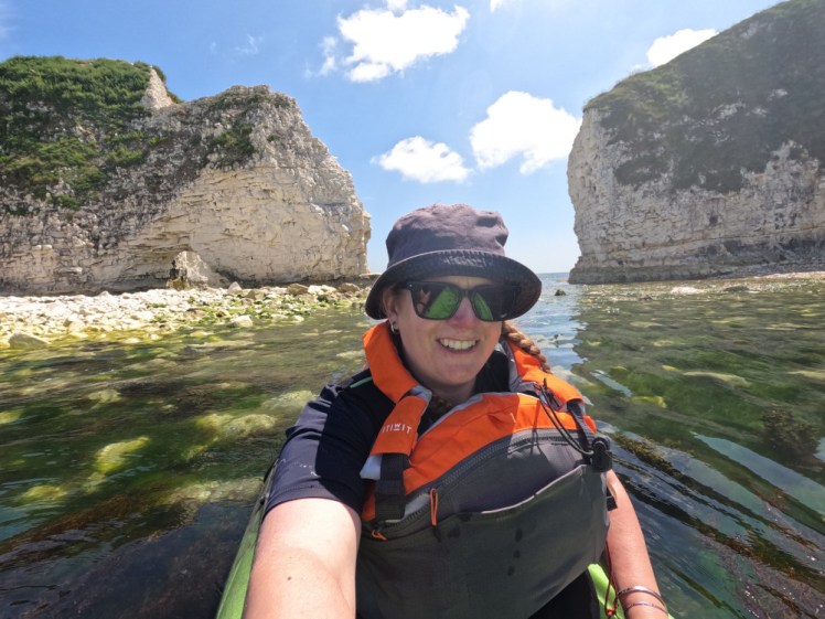 A selfie sitting a just-visible green kayak with the chalk formation Old Harry Rocks behind me.