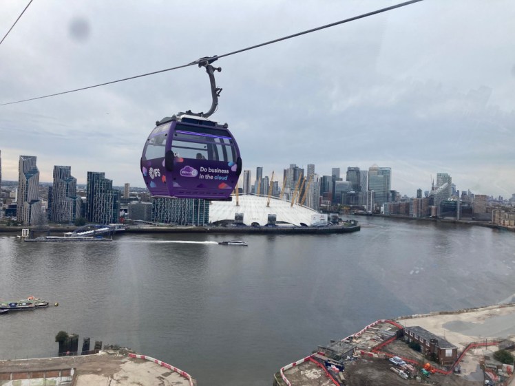 A view from the cabin looking towards the London Eye and the glass towers of the Canary Wharf district, with a purple cable car cabin hanging right in the middle - plus an annoying spot of dirt on the cabin window!