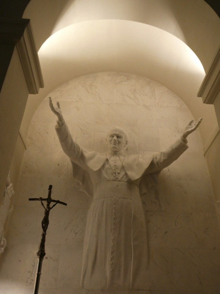 Pope John-Paul II in sculpture form, apparently coming out of the church wall, arms raised in blessing.