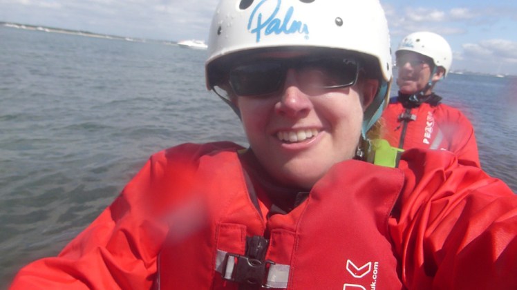 Me in another kayak out at sea, this time a two-person with my partner sitting behind me. We're both wearing red jackets and buoyancy aids and white helmets. The camera is splattered with water droplets.