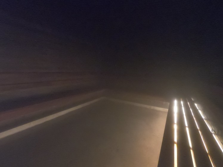 Inside the steam room. It's a square empty room, dimly lit and full of steam but you can just make out wooden walls. On the right-hand side is a bench made of thin planks of wood. Bright light glows from underneath it making four bright lines across the room.