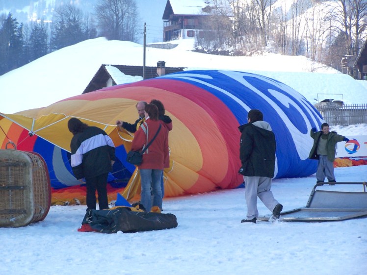 A bright-coloured stripy balloon lying on its side in the snow as the inflating process gets underway.