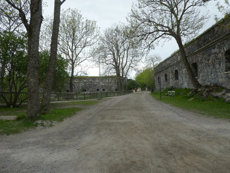The path, now dust and gravel, running up between two sets of defensive walls. They're not very high but they're clearly very solid and they have small windows in them.