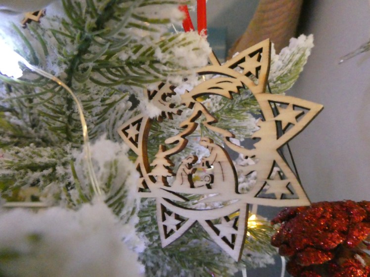 A wooden star-shaped ornament with the Holy Family in the middle under a Christmas tree.
