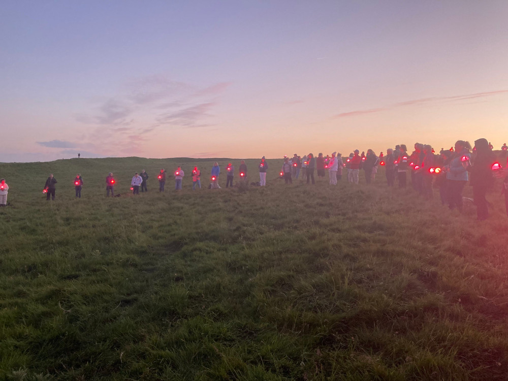 Team Red standing in a circle on the hilltop. The sky is now pastel shades of twilight purple and orange. Most of Team Red are holding a bright pink light now.