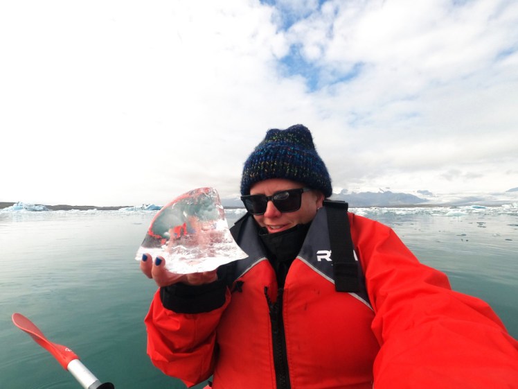 A selfie on the water. I'm holding up a large piece of crystal-clear ice about the size of my head but shaped like a shark fin.