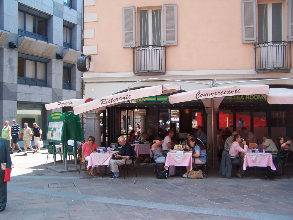 A cafe on a street corner, on the ground floor of a pastel apricot building. It has pale pink umbrellas describing it as a pizza restaurant. Did we have lunch here?