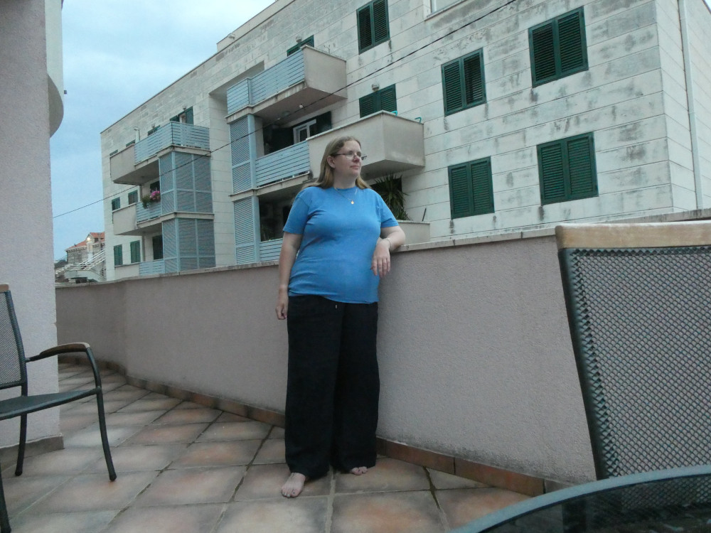 Posing on my terrace, deliberately not looking at the camera, wearing a plain blue t-shirt and navy linen trousers and bare feet because this is the cleanest terrace that ever existed.