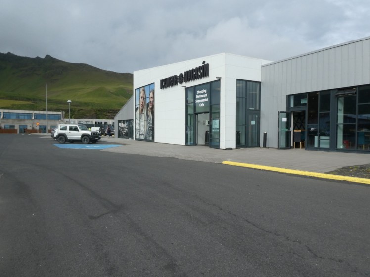 The shopping centre across the road, a white building with a big glass door, next to a grey building that looks, in a way, a bit more temporary.