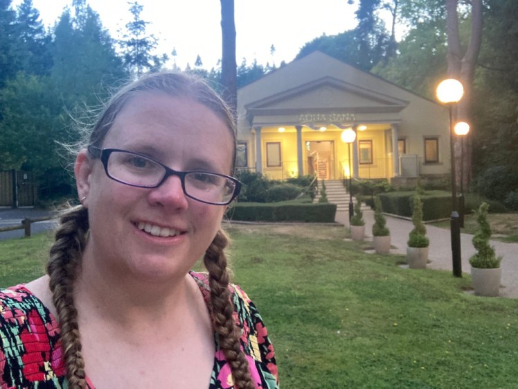 Selfie outside Aqua Sana's Classical style facade. My hair is wet and in two plaits and I'm wearing a colourful flowery dress. I look distinctly damp.