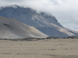 An expanse of pumice-covered Highlands, at the foot of Askja, a volcano with clouds sitting on its top.