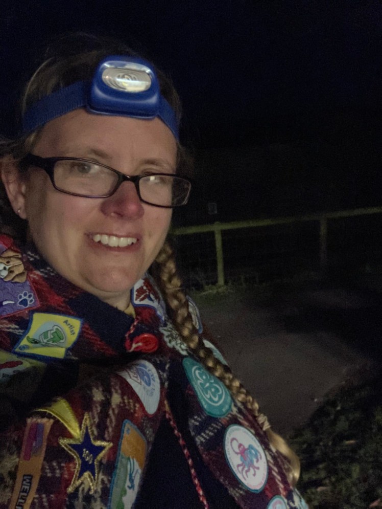 A bad selfie taken with the flash in the dark. I'm wearing a headtorch and my camp blanket, which is covered in badges.
