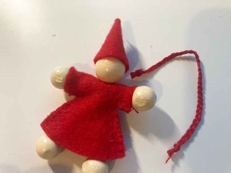 The nisse lying on my white desk with a length of plaited thread next to it.