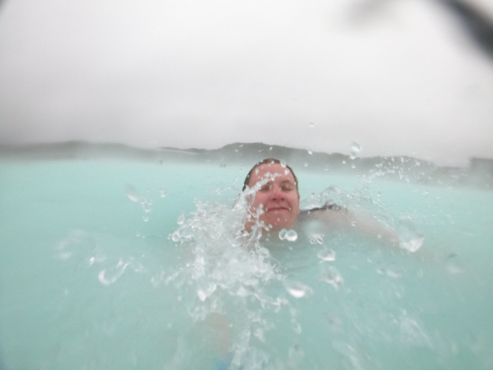 Me attempting to swim in the Blue Lagoon while a wave splashes across my face. It's still very cloudy and even the edges of the lagoon are a bit fuzzy behind me.