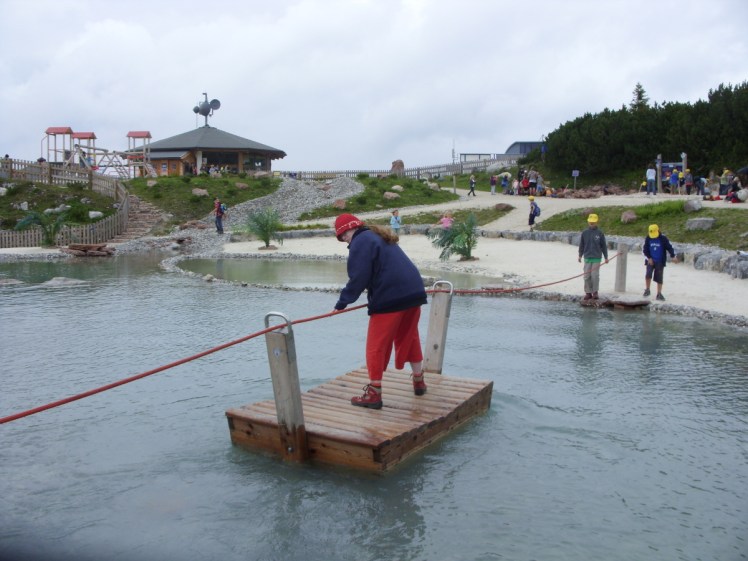 I'm standing on a wooden raft in the middle of a pond. There's a rope stretched across the pond which feeds through a