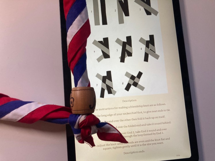A chapter with an illustration showing how to tie a friendship knot. My international neckerchief is lying next to the tablet, with its carved wooden woggle and friendship knot lying on the tablet.