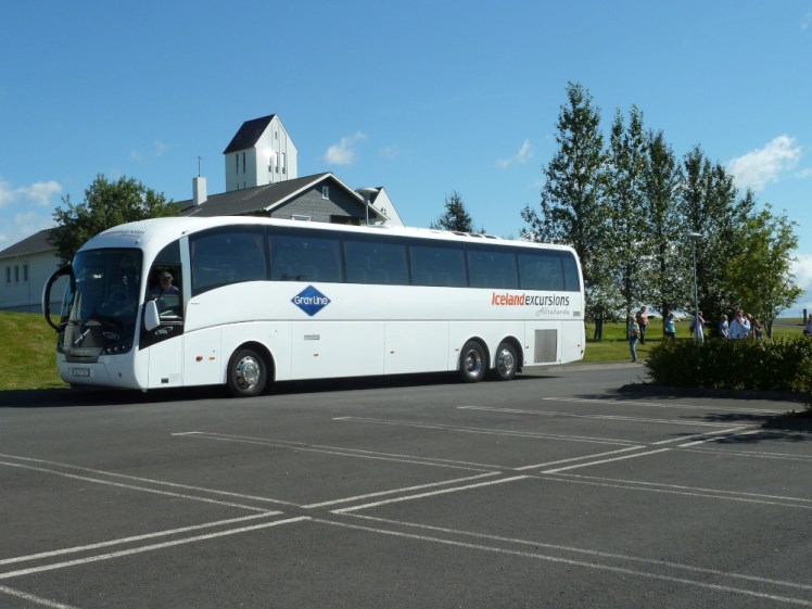 A Grayline coach, white and sleek, parked outside the church at Skalholt.