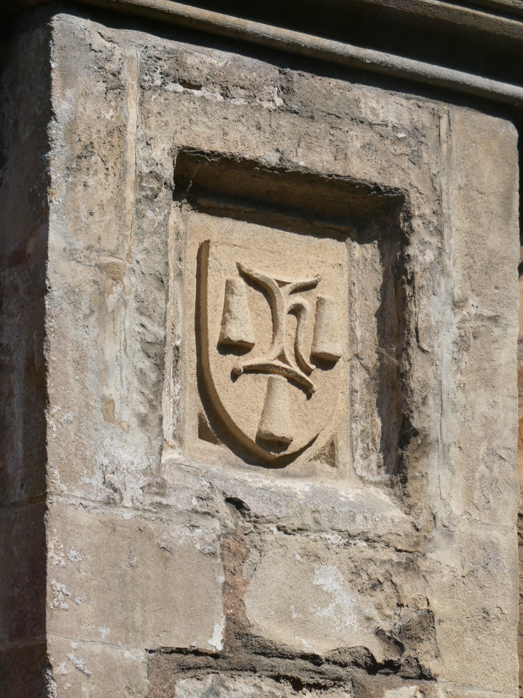 The arms of Hugh Sugar in a plaque in the side of one of the houses in Vicar's Close. There's a thing in the middle that might be a stool or a scale but around it are three cones. These are sugar, for his surname.