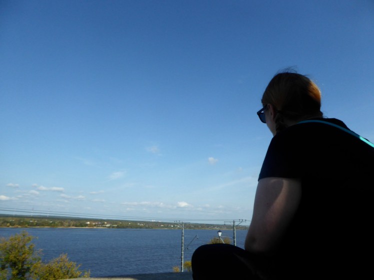 A selfie in Perm. The camera is just behind me on a mini tripod so you can see the river I'm looking at, my left arm and my back. I'm wearing a black t-shirt and sunglasses.