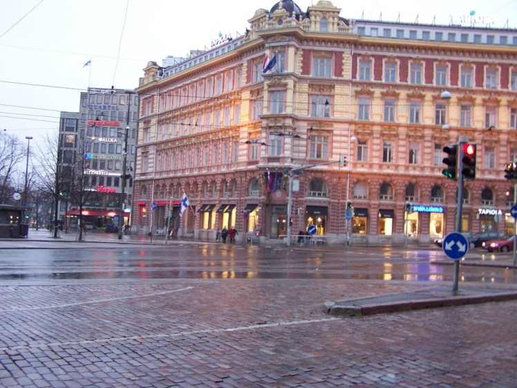 A wet afternoon in Helsinki: cobbled streets and elaborate buildings, with the various street lights reflecting on the wet cobbles.