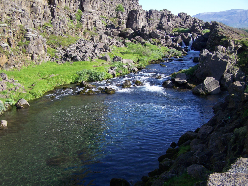 The Drowning Pool, a deep blue pool at the foot of the cliffs, with a river bubbling gently into it.