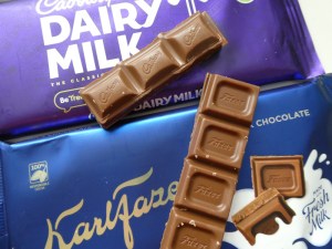 Dairy Milk in its purple wrapper with Karl Fazer in its blue wrapper. There is a stick of each lying on top.