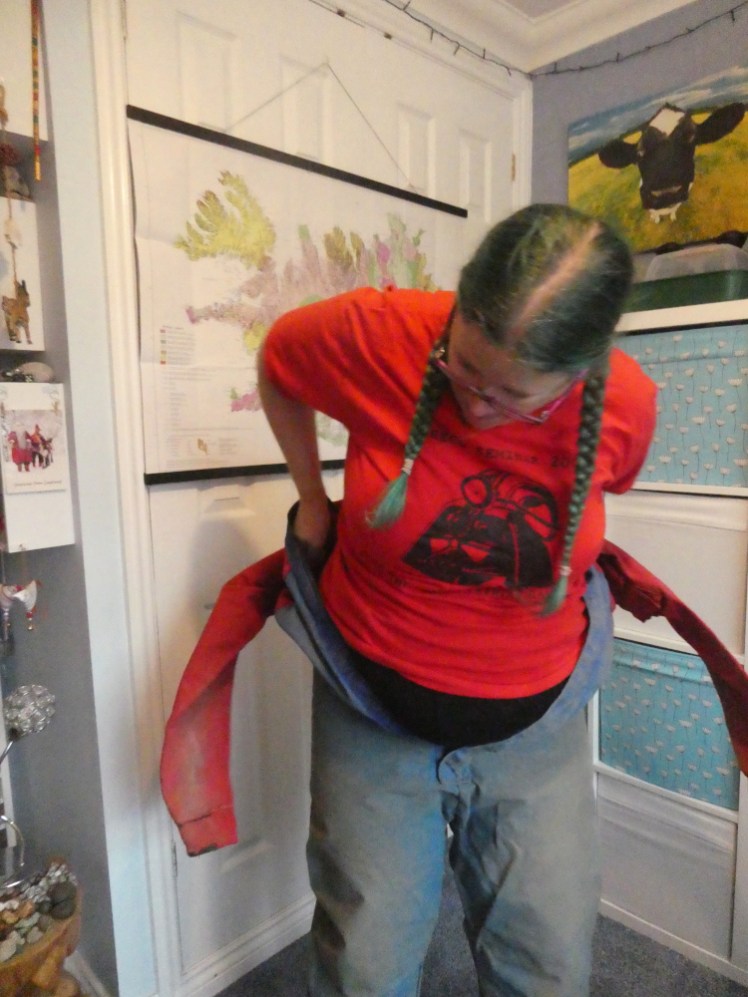 Me, wearing a red caving t-shirt, struggling to get into a red and blue cordura caving oversuit that's quite a bit too small these days.