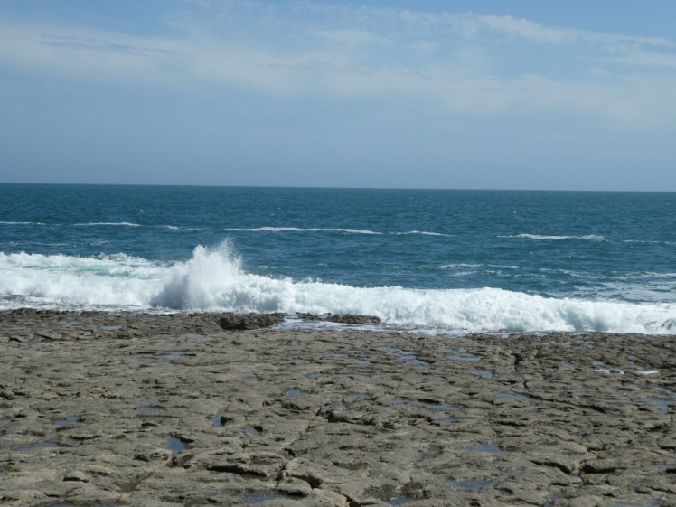 A large wave crashing up and onto the Ledge, which is a limestone shelf a couple of feet above the water level.