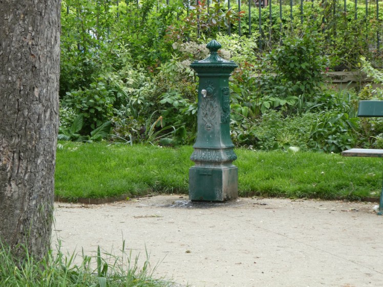 A green-painted wrought iron water fountain in a park.