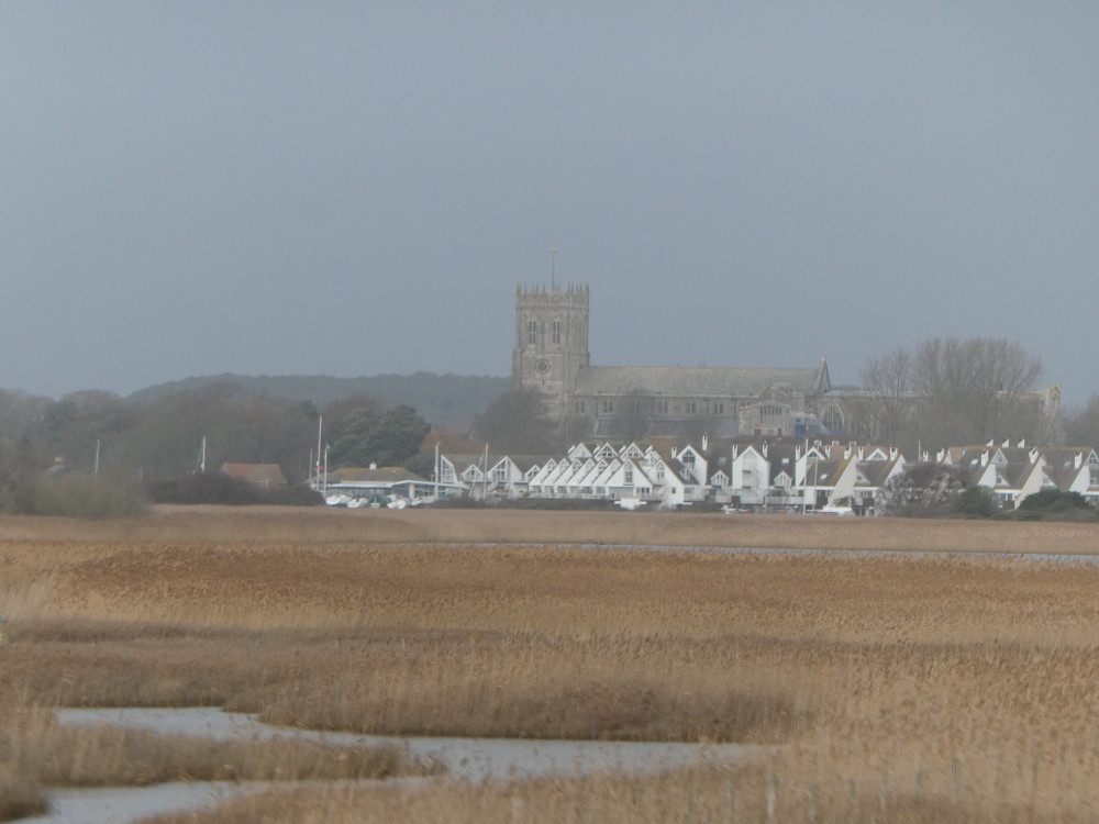 In the slight haze of distance stands Christchurch Priory, a grey Norman-style church. In front of it are the white-fronted houses along Priory Quay and the whole lot is hiding behind an extent of wetlands, reeds, grasses and a thin sliver of harbour. All the vegetation is in its winter shade of orangey-brown.
