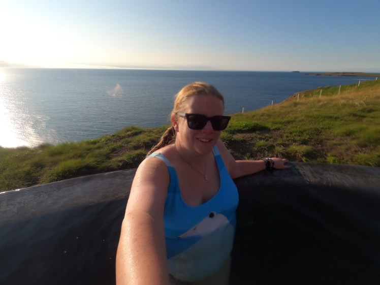 A selfie with my polar bear swimsuit in full view. Behind me, you can see the grassy cliffside and now you can see how far below the fjord actually is.