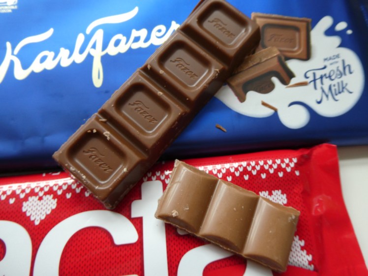 The two bars of chocolate lying next to each other with their chocolate lying on top next to each other. It's very obvious that Lacta is a lot paler than Fazer and the pieces are much smaller.