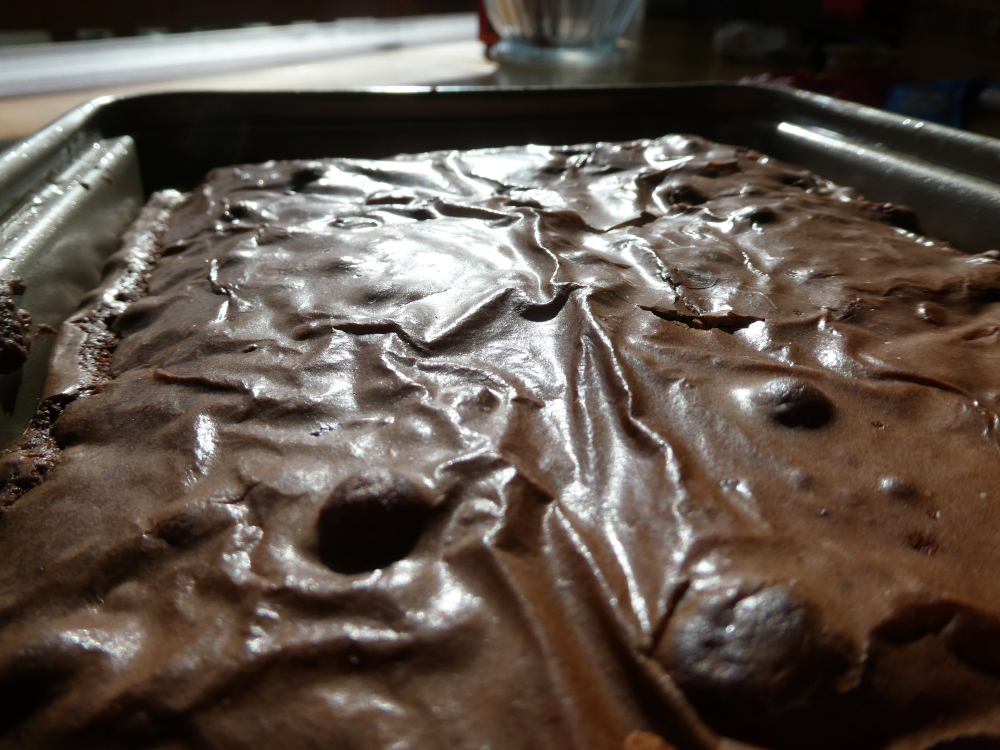 A close-up of the surface of a tray of brownies. These are a packet mix which you make with oil, water and an egg so the surface is a bit shinier than brownies would properly be.