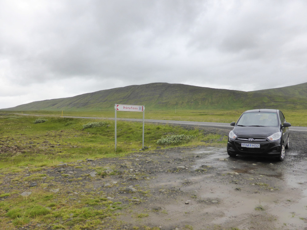 A small black Hyundai parked on a patch of gravel next to some grassy gravel. It's either raining or has been raining recently.