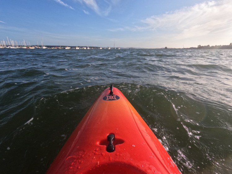 A red kayak plunging through some small but forceful waves.