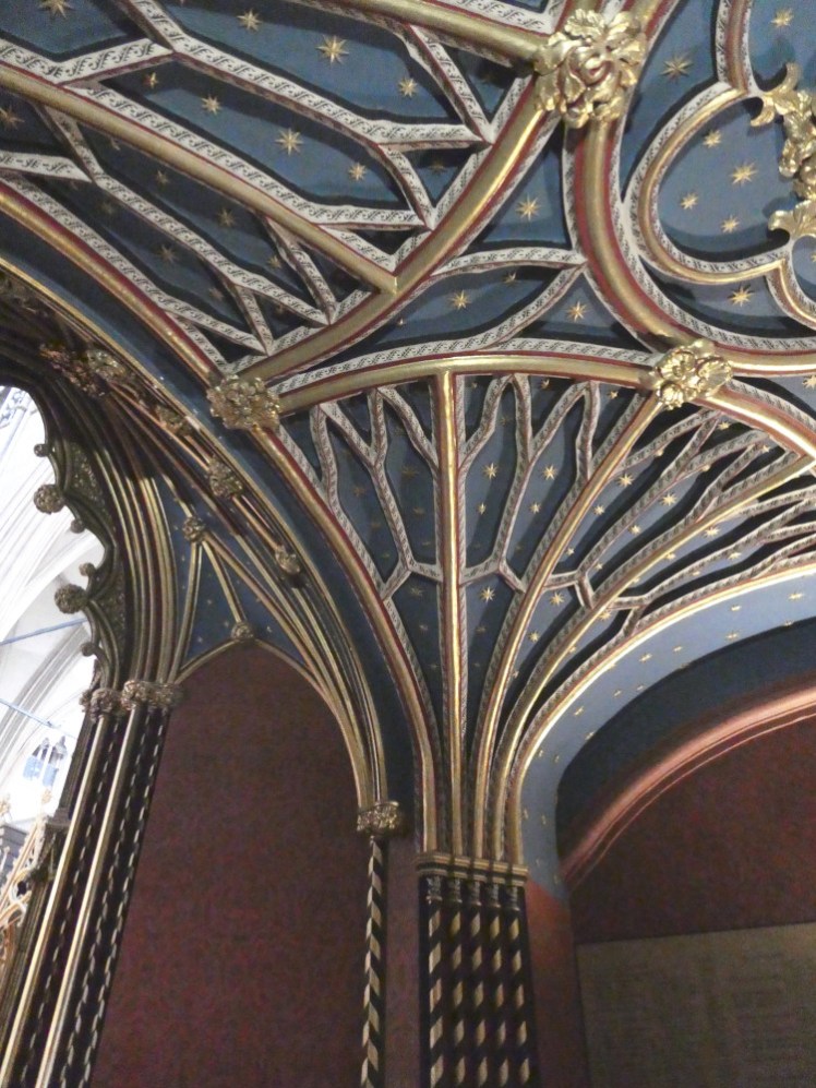 The colourful archway into the quire, all gold ribs and blue ceiling splattered with stars and striped uprights in red and gold.