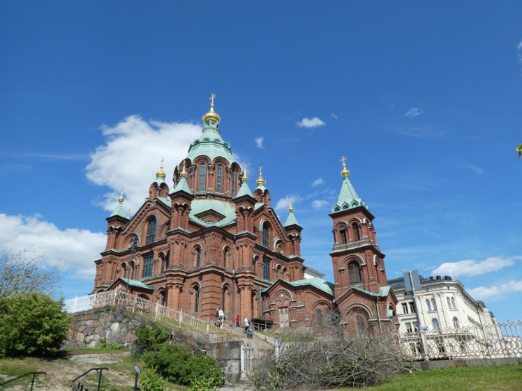 Uspenski Cathedral, red brick and green domes on the side of a shrubby hill, towering over the east side of the city.