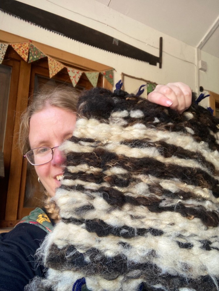 A selfie holding up my finished mat. It's very fluffy and has striped of white and dark brown.