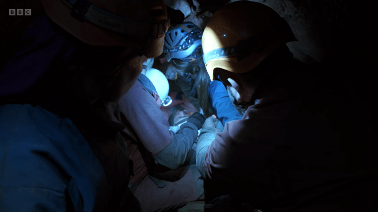 Recreating the rescue: a lot of cavers crammed into a very tight space in the cave, all helmets and spotlights.