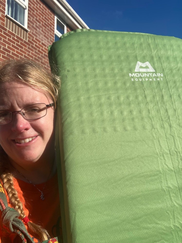 A selfie holding up a green self-inflating mat. At the top, you can make out a grid pattern within the mat which becomes more of a stripe further down.