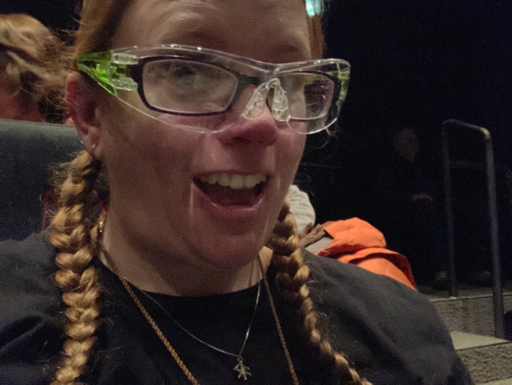 A selfie in the darkened theatre. I'm wearing a black t-shirt and have my hair in plaits but I'm also wearing a pair of protective goggles with green arms over my normal glasses and look delighted about it.
