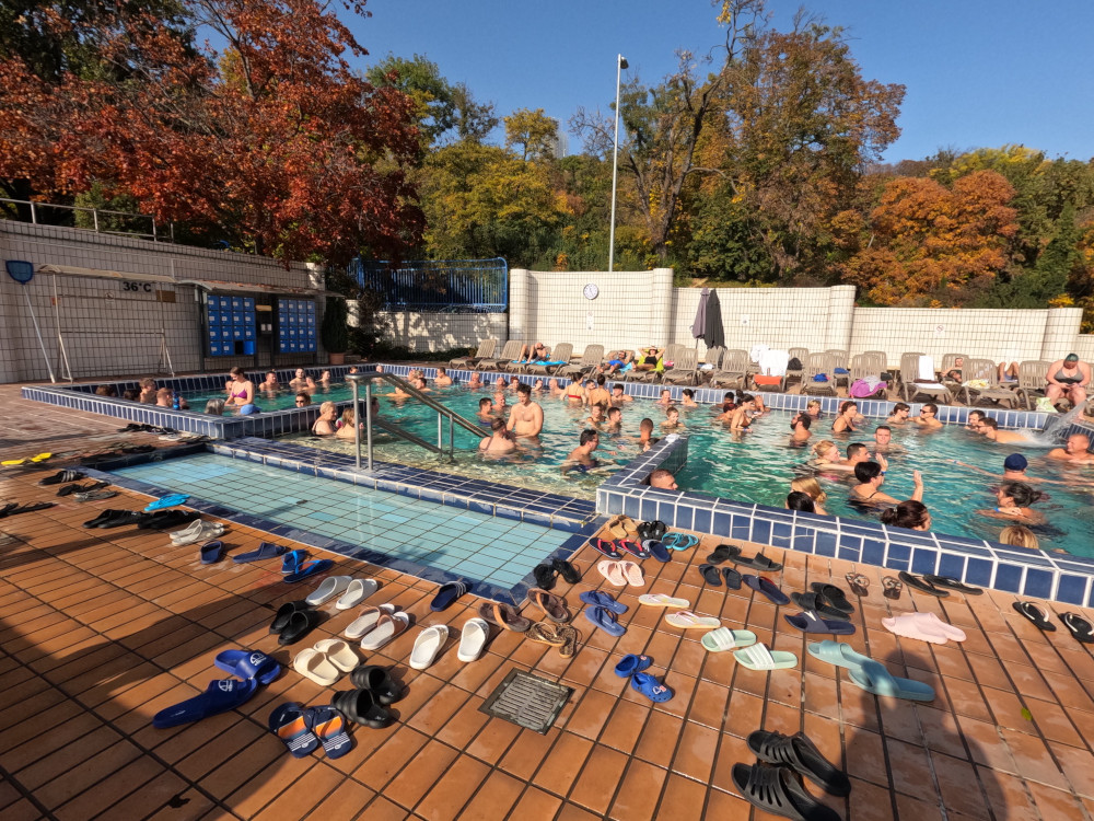 Lots of pairs of flipflops by the edge of an outdoor thermal pool.