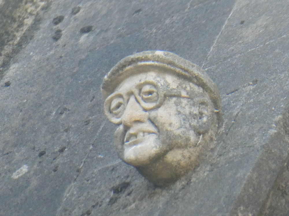 A small stone head on the outside of the Chapter House. It's wearing a flat cap and glasses, has quite prominent teeth and looks profoundly non-celestial.