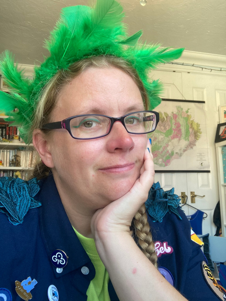 A selfie in full Hawk outfit for Camp Wildfire. I'm wearing a navy shirt covered in badges and with blue-green "wings" on my shoulders. I'm also wearing a bright green feather headdress and dark green liquid eyeliner.