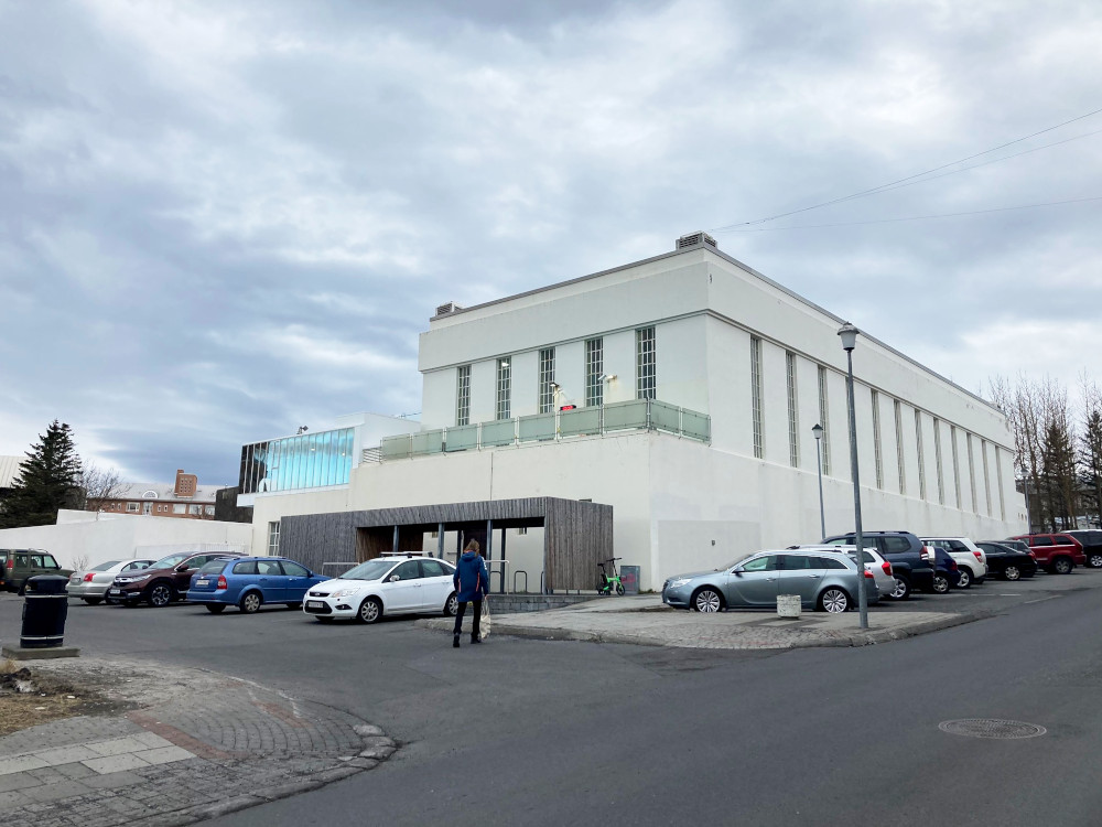 Sundhollin, a squarish white Art Deco building with a balcony on the front surrounded by greenish opaque glass. In front is a car park.