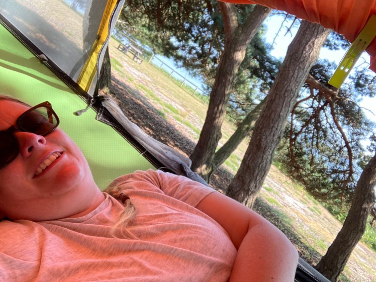 Me in a hammock (actually, it's a tree tent with the cover folded up) wearing a grey t-shirt. Behind me, you can see through the trees to a scrubby beach and blue sea.