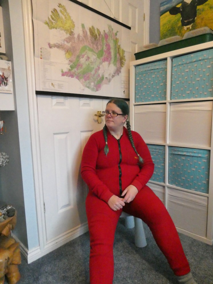 Me, sitting in a tiny chair, wearing a red all-in-one fleece caving undersuit. It's a thick tough onesie.