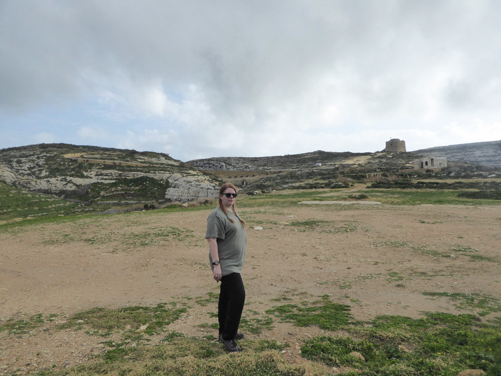 A selfie on a dusty bit of land by the sea in Malta. I'm wearing my grey-green Taylor Swift t-shirt which makes me merge into the grey-green-orange background a bit.