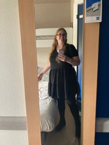 A really bad mirror selfie in a pretty bad hotel. I'm wearing a short-sleeved black dress with a fairly short skirt that flounces out a little, black tights and boots and for once, I have my hair down.
