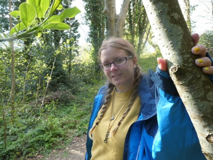 Me in the woods, wearing a yellow jumper and blue raincoat. The whole picture is in my branding colours. As usual, my hair is in plaits.